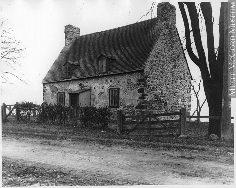 Photo noir et blanc montrant une maison de pierre ancienne le long d’un chemin de terre