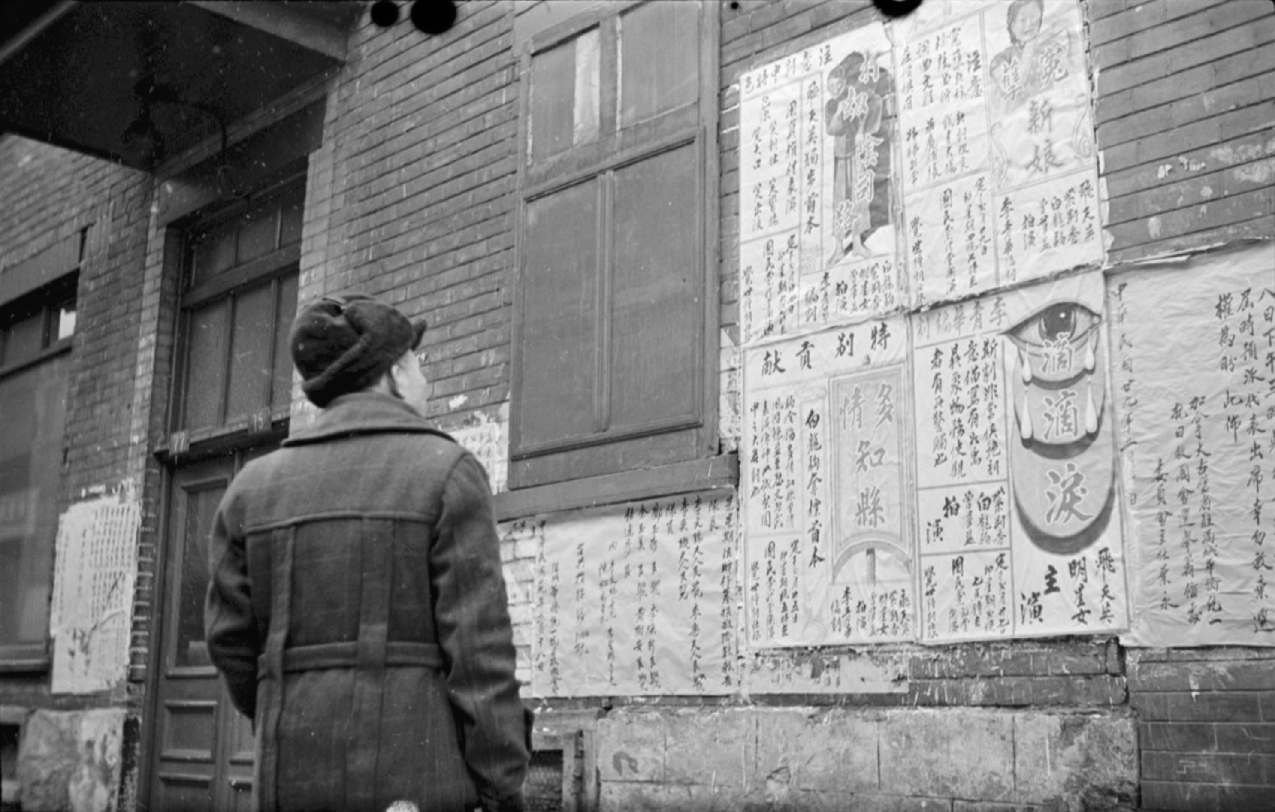 Un homme lit des affiches en chinois sur le mur d'un édifice