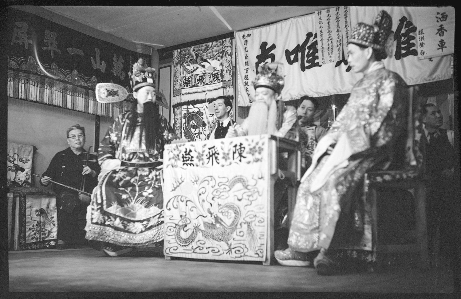 Photo en noir et blanc de six comédiens et musiciens d’origine chinoise sur une scène de théâtre. 