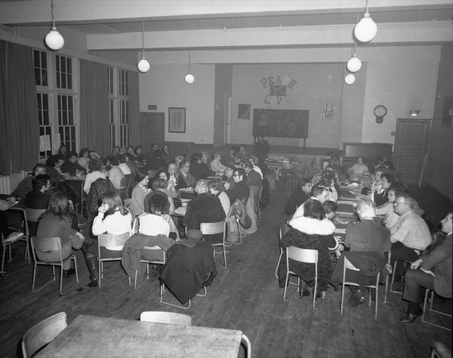Une cinquantaine de personnes sont réunies dans une salle et regroupées autour de tables.