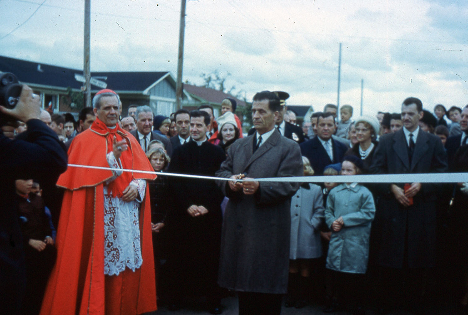 Un homme, avec le cardinal Léger à ses côtés et une foule d’hommes, de femmes et d’enfants derrière lui, s’apprête à couper un ruban pour inaugurer un boulevard.