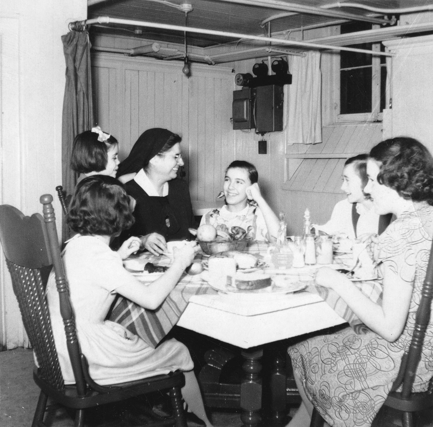 Une femme riant, portant le voile, assise à une table avec cinq enfants. 