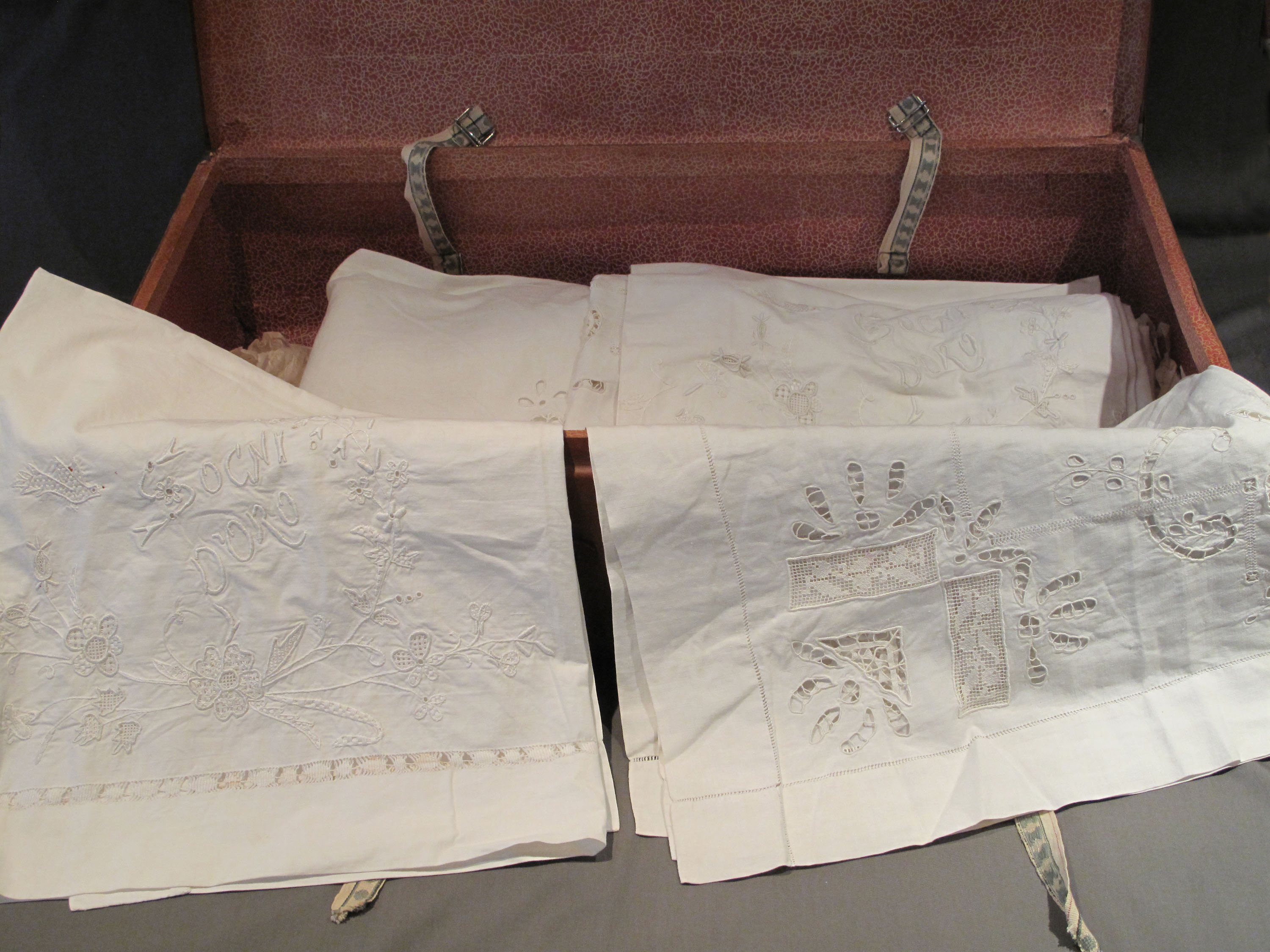 Valise ouverte d’une immigrante italienne contenant quatre couvre-oreillers et trois draps en lin.