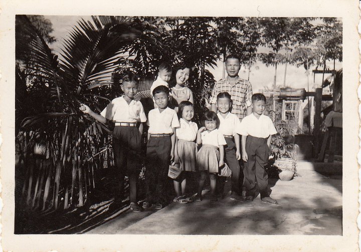 Photo en noir et blanc d’une famille de sept enfants avec la mère et le père. La mère tient le plus jeune dans ses bras. 