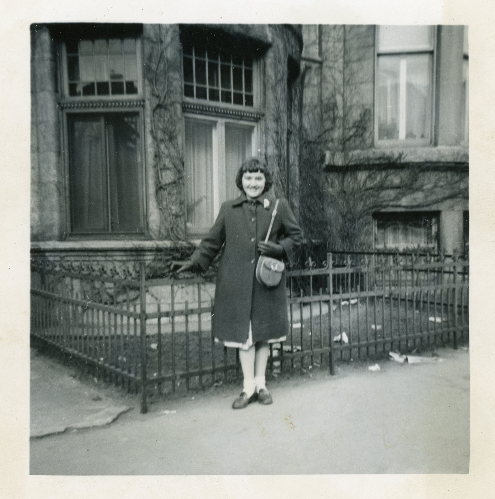 Photo en noir et blanc d’une jeune femme prenant la pose debout sur le trottoir devant la maison familiale.