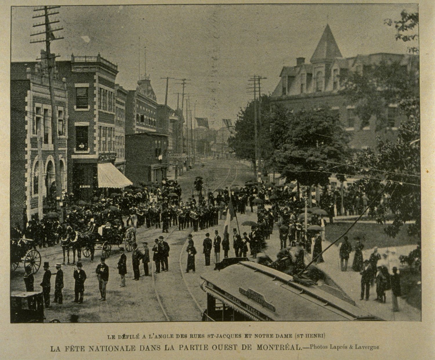 Photo ancienne d'une foule sur une place lors d'un défilé où on aperçoit un tramway.
