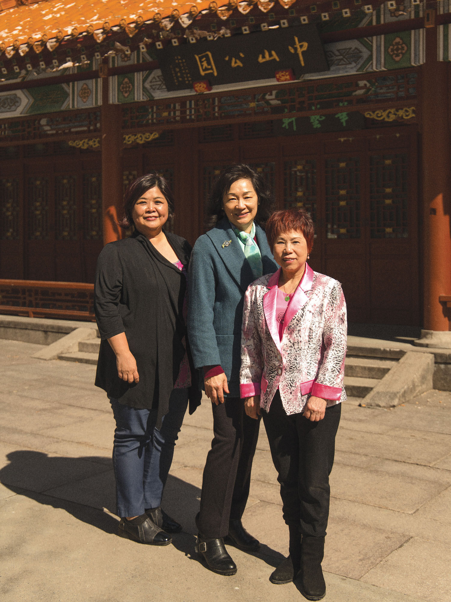 Photo couleur plein pied de trois femmes souriantes posant debout sur la place Sun-Yat-Sen dans le Quartier chinois. 