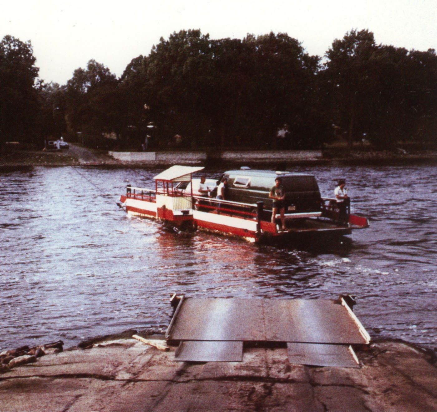 Photo couleur montrant un traversier avec deux véhicules à son bord sur une rivière. On aperçoit les deux rives.