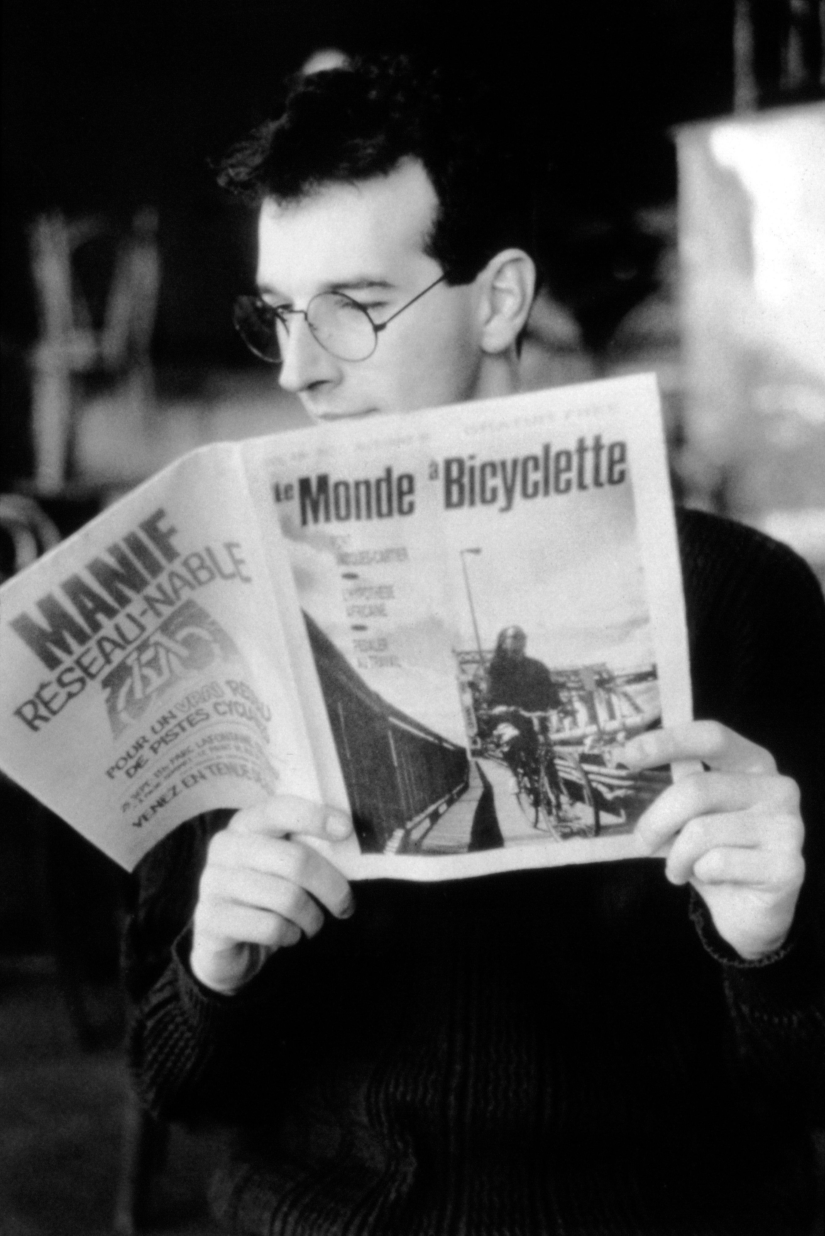 Homme lisant le bulletin Le Monde à bicyclette