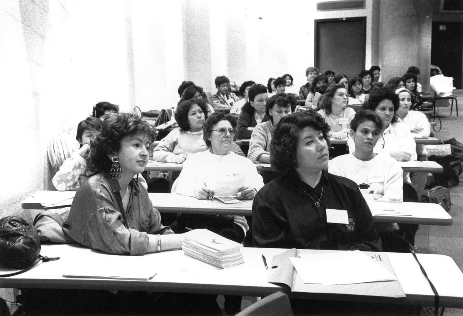 Photo noir et blanc d’un groupe de femmes assises et attentives dans une salle de conférence. 