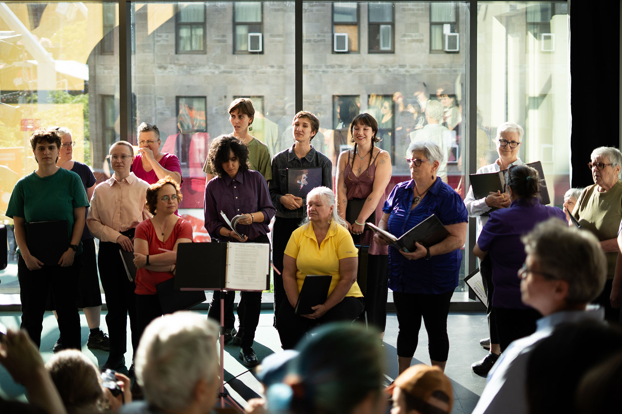 Chorale d’une quinzaine de femmes devant une grande baie vitrée.