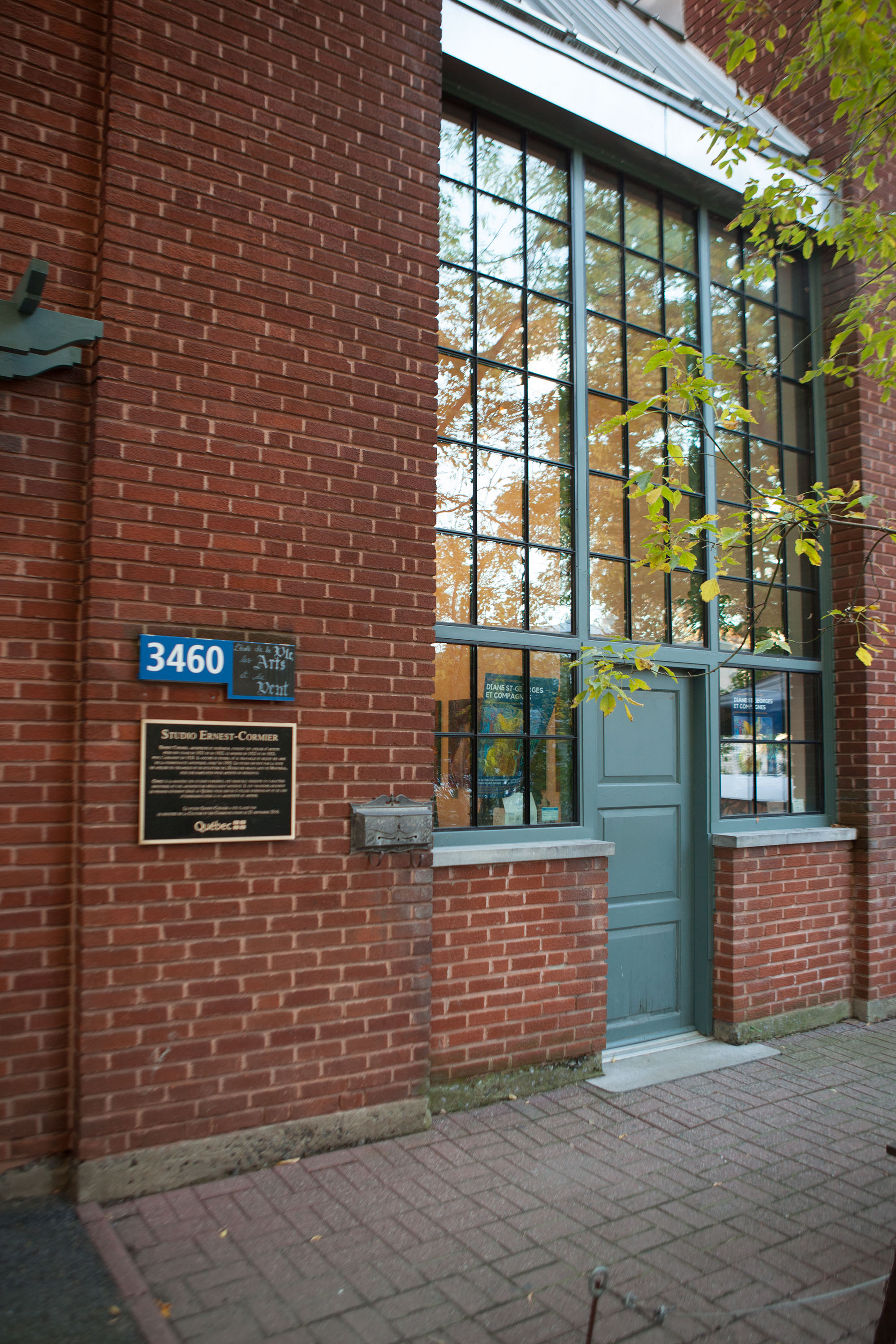 Photo couleur en plan rapproché de la façade d’un bâtiment de brique rouge avec une grande verrière au-dessus et autour de la porte d’entrée. 