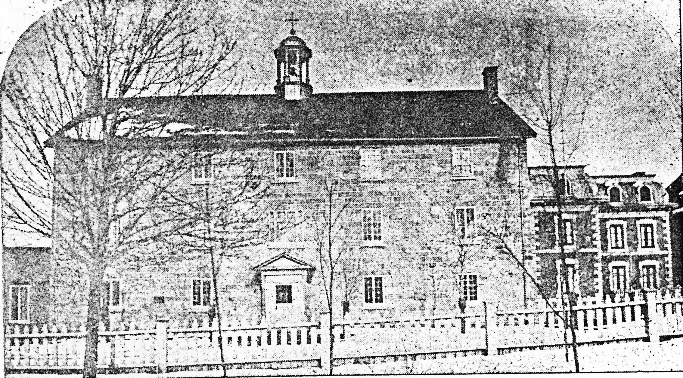 Photographie en noir et blanc représentant un édifice de trois étages, au toit mansardé, avec un clocheton.