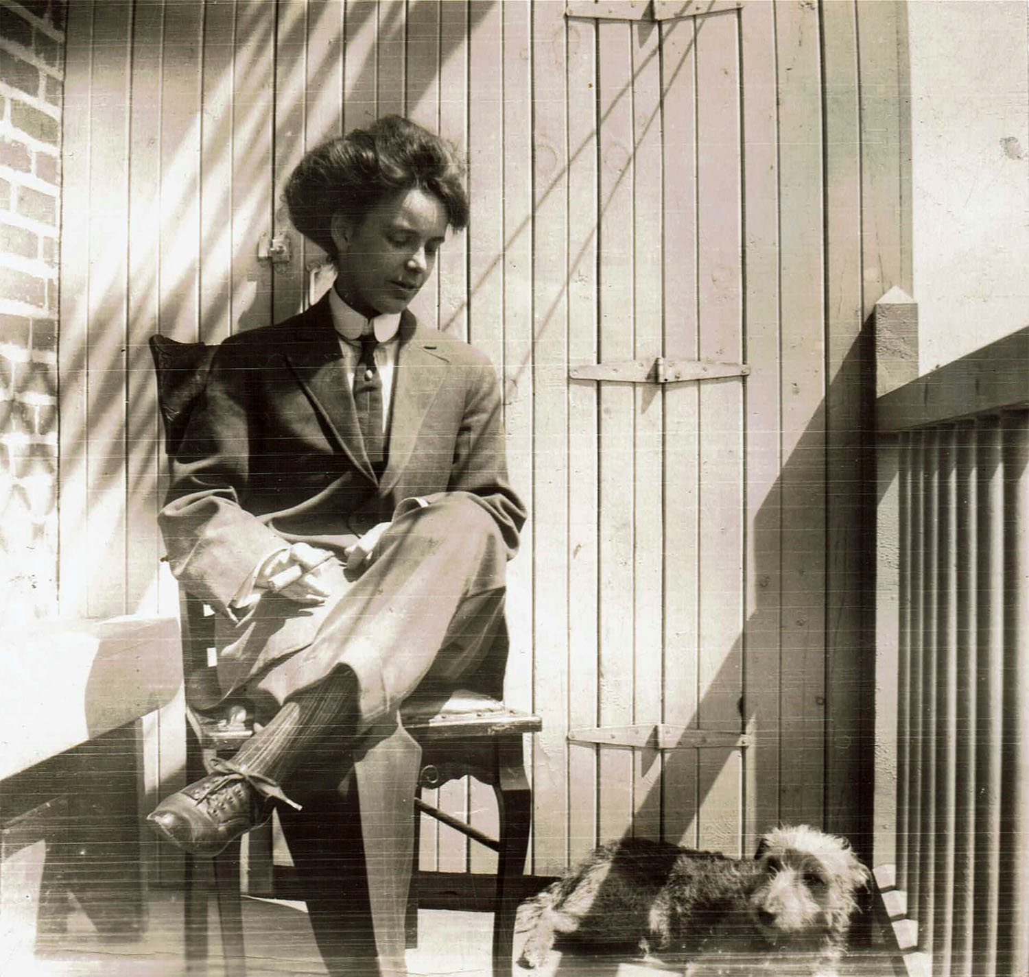 Jeune femme portant un veston et une cravate, assise sur un balcon d’appartement, avec à ses pieds un petit chien.