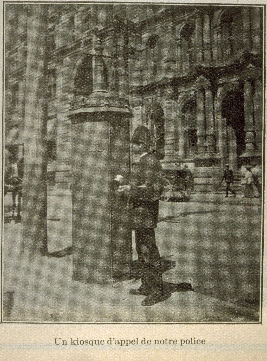 Photographie en noir et blanc tirée d’une coupure de journal. On y voit un policier en uniforme près d’une boîte d’alarme.