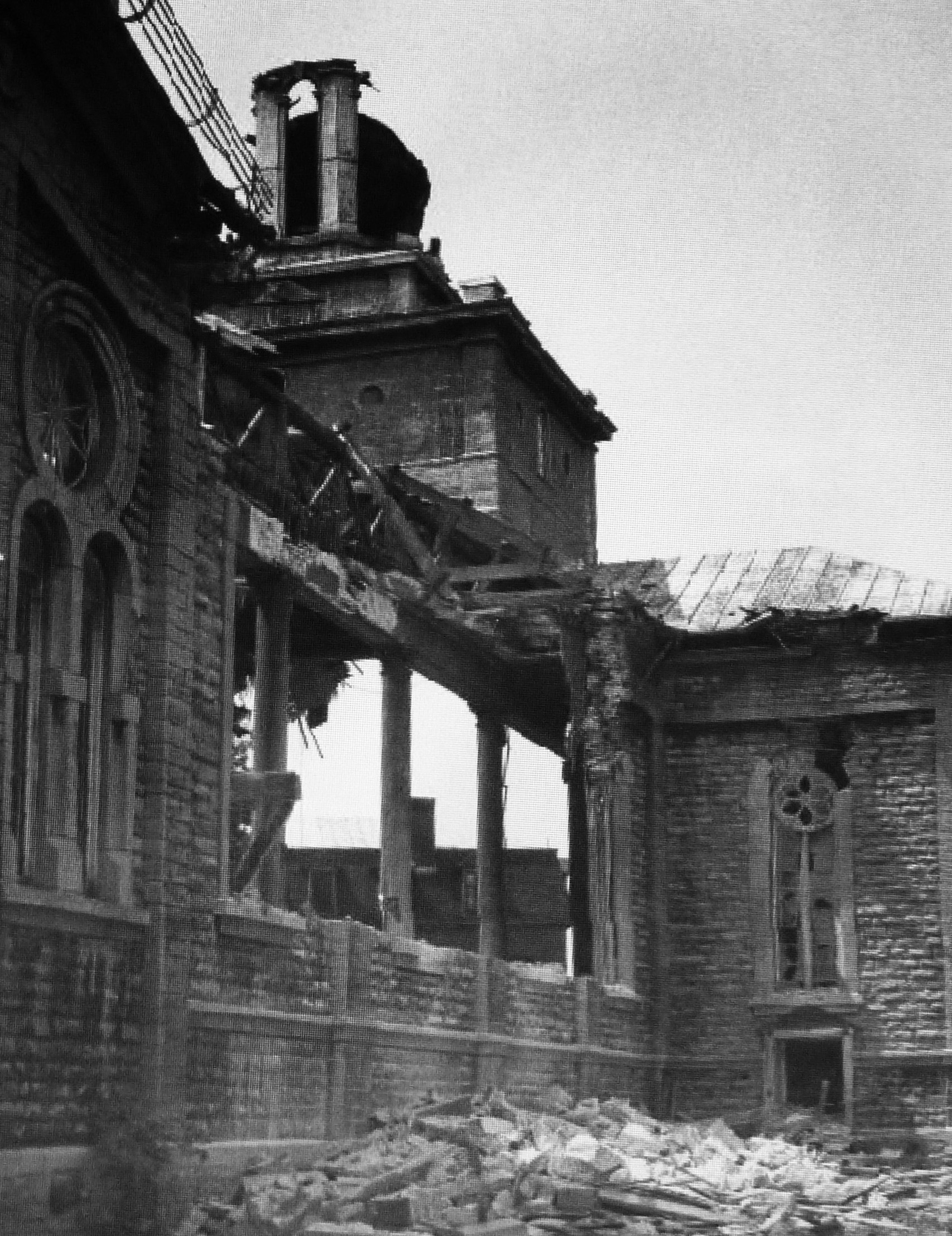 Photographie d'une paroi de l'église en démolition; des débris ornent le sol.