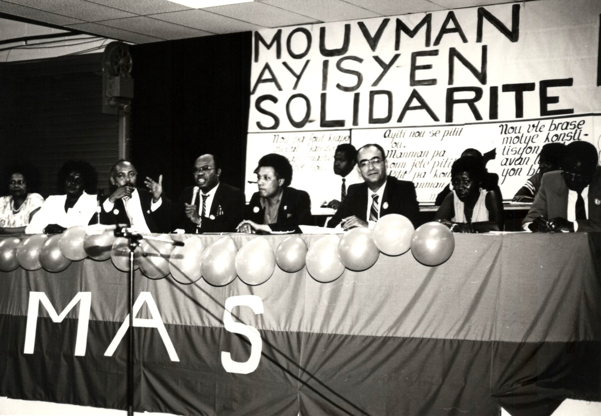 Des membres du Mouvement haïtien de solidarité sont assis derrière une table pour prendre la parole lors d'un événement