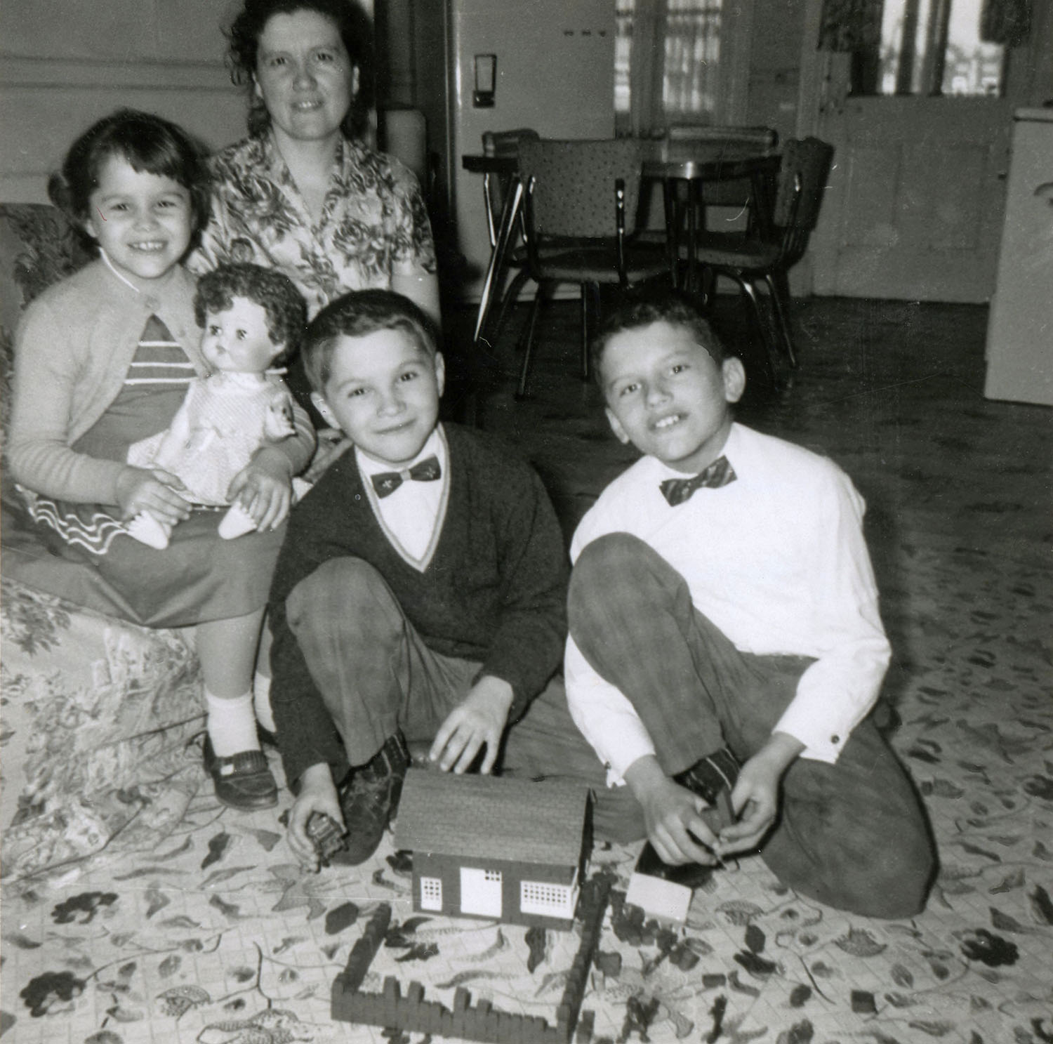 Une mère et ses trois enfants prennent la pose avec les cadeaux de Noël reçus dans leur salon. On voit la cuisine à l’arrière-plan. 