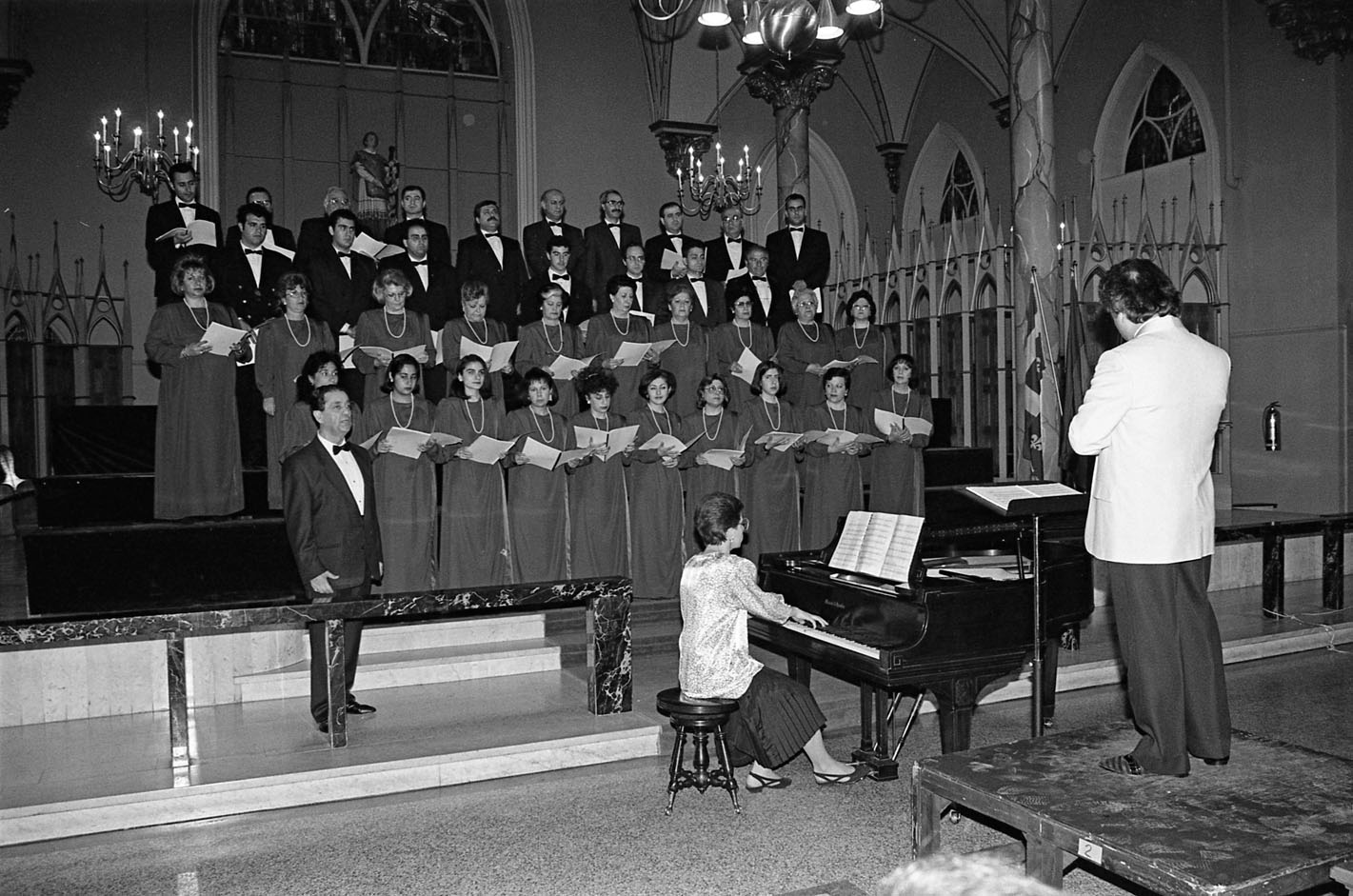 Une trentaine de femmes et d’hommes chantent dans une église. Une femme joue du piano.