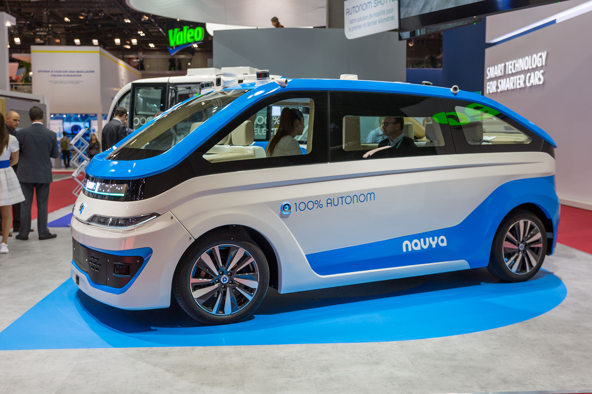 Photographie en couleur d’une voiture dans un salon de l’automobile. On peut lire sur la voiture 100 % autonom navya.