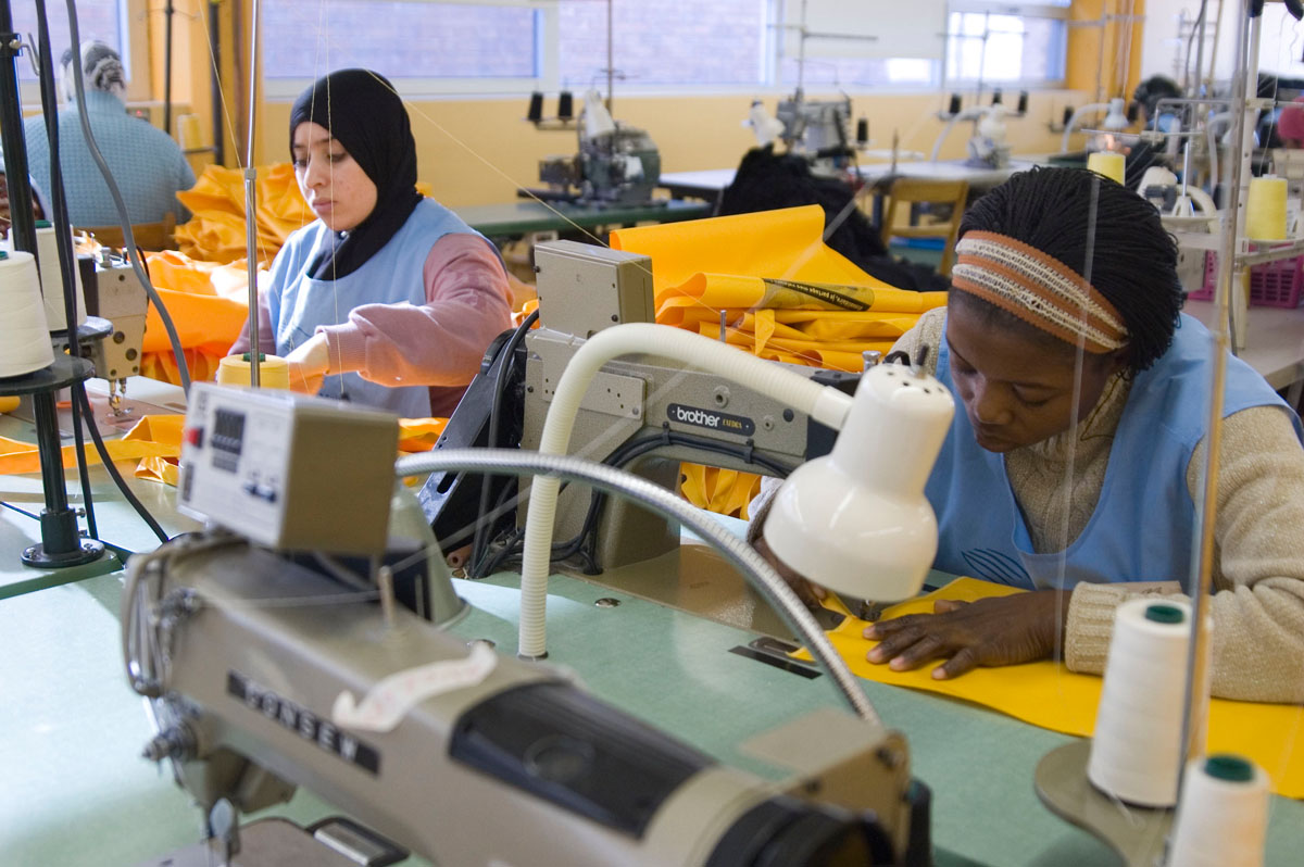 Gros plan sur deux femmes travaillant sur des machines à coudre industrielles dans un grand atelier. 