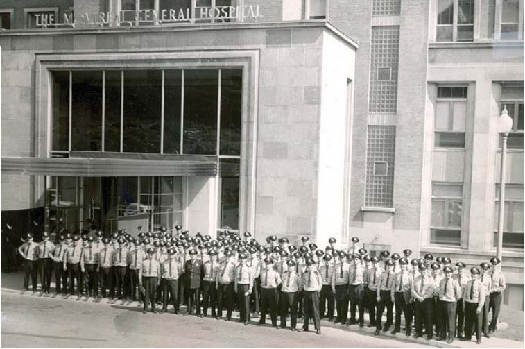 Photographie en noir et blanc d’un groupe de policiers en uniforme se tenant debout devant la porte du Montreal General Hospital.
