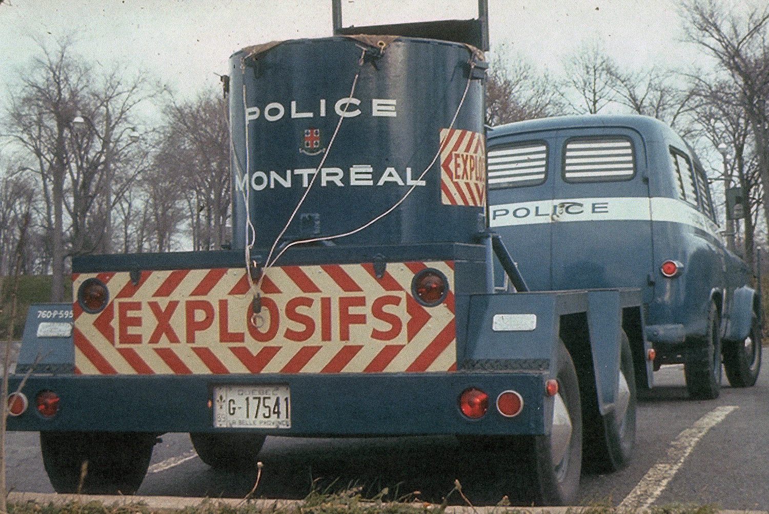 Photographie couleur montrant la partie arrière d’un camion bleu auquel est attachée une remorque sur laquelle il y a un grand contenant de métal cylindrique. Sur la porte de la remorque, il est écrit « explosifs » en lettres majuscules.