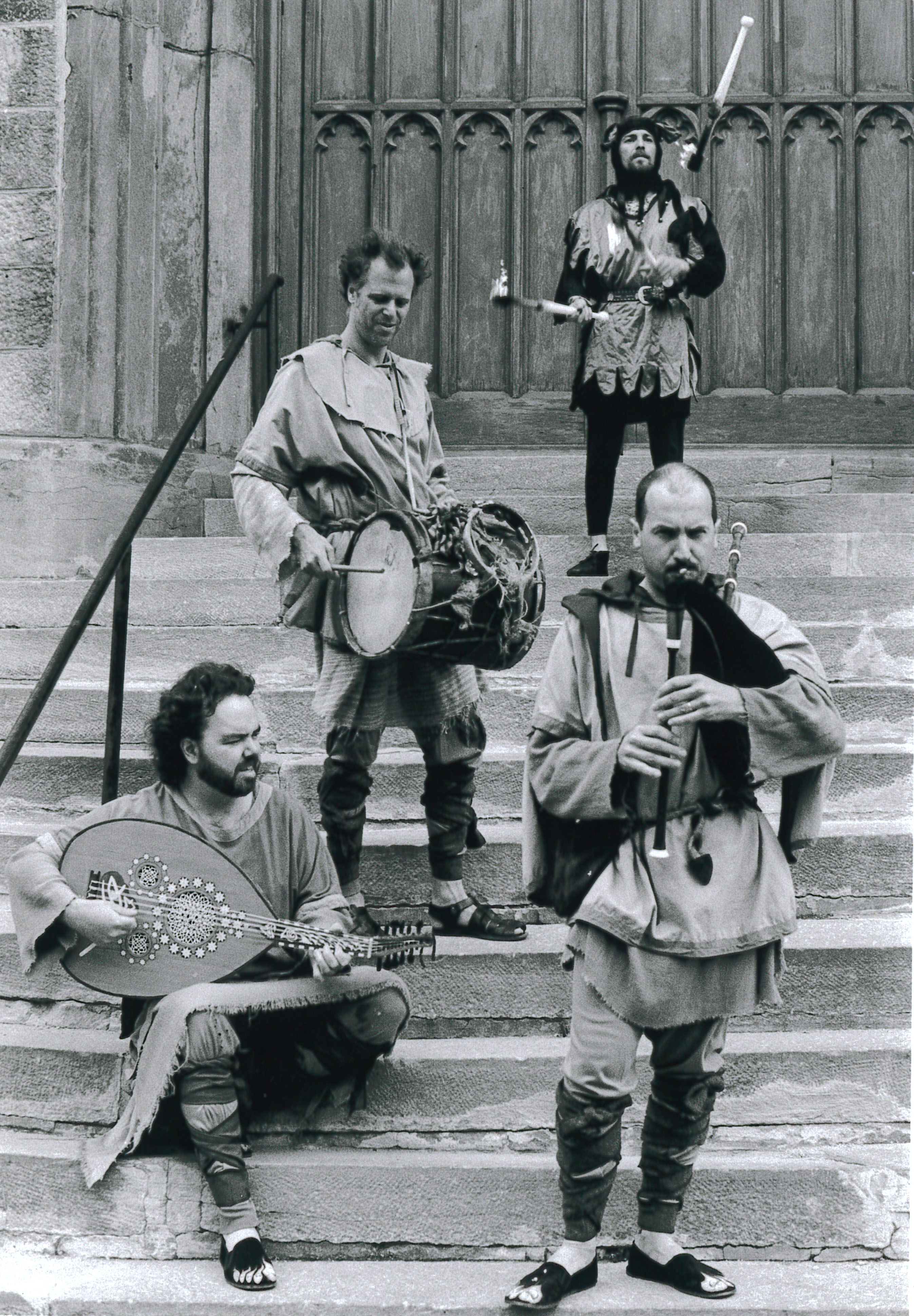 Quatre hommes jouent des instruments de musique sur les escaliers extérieurs en pierre d’un bâtiment.