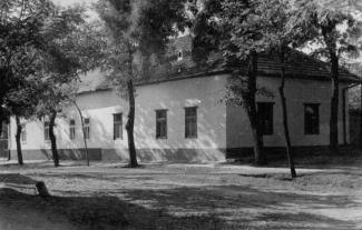 Photo en noir et blanc d’une grande maison rectangulaire entouré d’arbres.