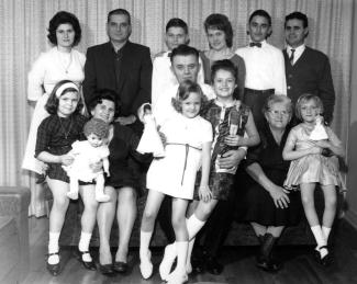 Photo en noir et blanc d’un groupe de personnes composé d’hommes, de femmes et d’enfants. Six sont debout à l’arrière, les autres sont assis devant. L’homme au centre tient deux enfants sur ses genoux.  