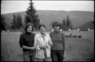 Photo noir et blanc de trois jeunes femmes se tenant par les coudes dans un paysage montagneux.