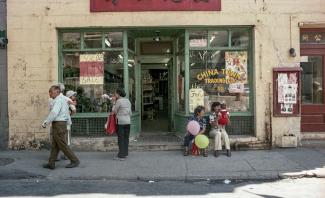 Photo couleur montrant la devanture d’un commerce du Quartier chinois avec des personnes assis devant ou circulant sur le trottoir