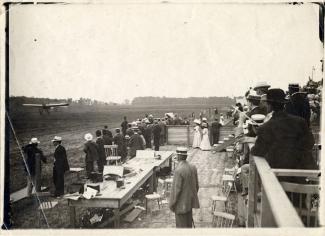 Vue éloignée en plongée, prise des estrades derrière l’équipe de la presse, lors de l’atterrissage du « Scarabée », avec à son bord le comte Jacques de Lesseps, à Pointe-Claire (Lakeside).