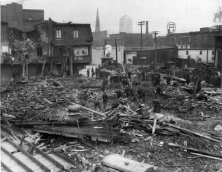 Site de l’écrasement d’un avion dans le quartier Griffintown. Plusieurs maisons sont complètement démolies. Des gens sont sur le site des maisons en ruine. 