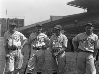 Photo en noir et blanc de quatre joueurs de baseball de l’équipe des Royals. Chacun s’appuie sur un bâton de baseball.