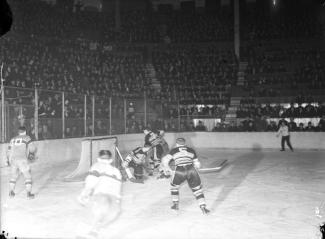 Photo en noir et blanc montrant des joueurs de hockey sur la glace et une foule nombreuse dans les gradins.