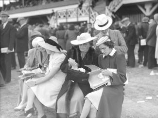 Photo noir et blanc montrant un groupe de femmes s'apprêtant à effectuer des paris sur le terrain de l'hippodrome Mont-Royal. Nous apercevons à l'arrière-plan une partie des installations du champ de course.