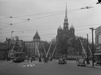 Photo ancienne d'une place où circulent un tramway et des voitures des années 1940 à un passage à niveau.