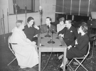 Un groupe de trois femmes et trois hommes assis autour d’une table dans un studio de radio.