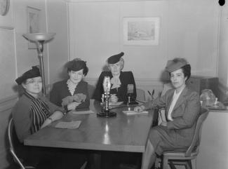 Photo noir et blanc de quatre femmes assises autour d’une table, un micro est posé au milieu de la table. 