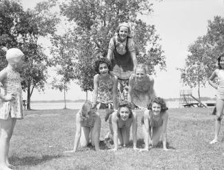 Six adolescentes forment une pyramide sur la pelouse d'un parc et deux autres jeunes filles les regardent