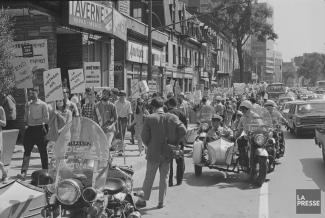 Manifestation au centre-ville, beaucoup de personnes ont des pancartes « Le Vietnam aux Vietnamiens » et autres messages anti-guerre. Des policiers à moto sont à l’avant-plan le long de la foule.