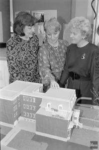 Trois femmes observent la maquette d’une grande maison.