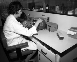 Une femme portant un sarrau est assise à un bureau dans un laboratoire et manipule un appareil.