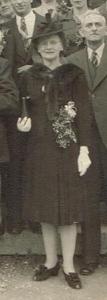 Photo noir et blanc recadrée autour d’une femme en format plein pied. Elle est entourée d’hommes et de femmes vêtues pour une occasion spéciale.