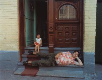 Un homme fait la sieste sur le pas de la porte sous le regard d'une petite fille.