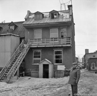 Un homme tient une pancarte devant l'arrière d'une maison l'identifiant pour l'expropriation