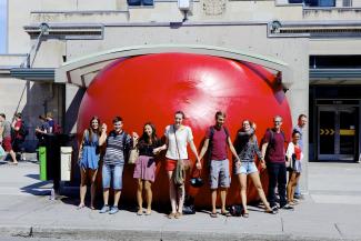 Neuf personnes se tiennent la main devant une grosse ballée gonflée orange devant une station de métro