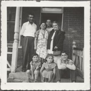 La famille Fratino sur le pas de la porte de leur maison sur la rue Clark. Ils sont quatre debout et trois enfants assis. 