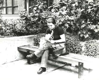 Fotografia a preto e branco de uma mulher a ler, sentada num banco no exterior de um edifício.